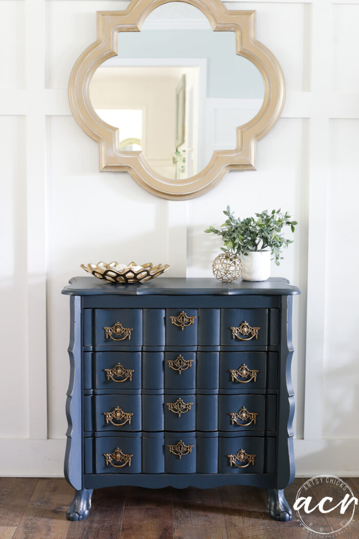 blue dresser with decor on top under gold mirror