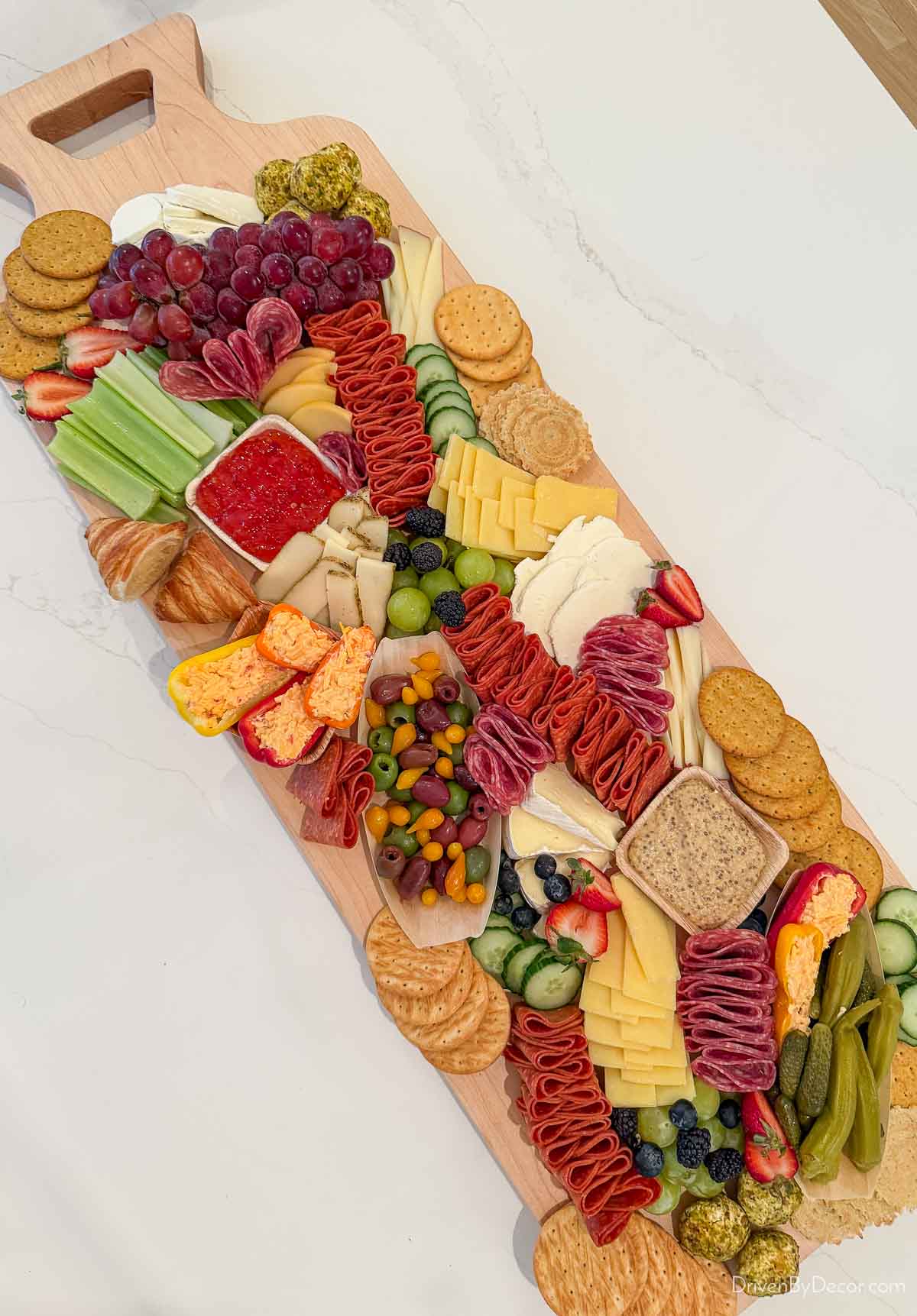 Long charcuterie board loaded with meats, cheeses, fruit, and more